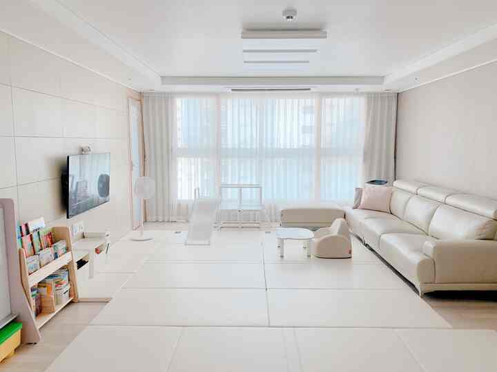 Bright beige and cream-toned living room featuring large foldable mats, children's slide, and cream leather sofa with a serene atmosphere