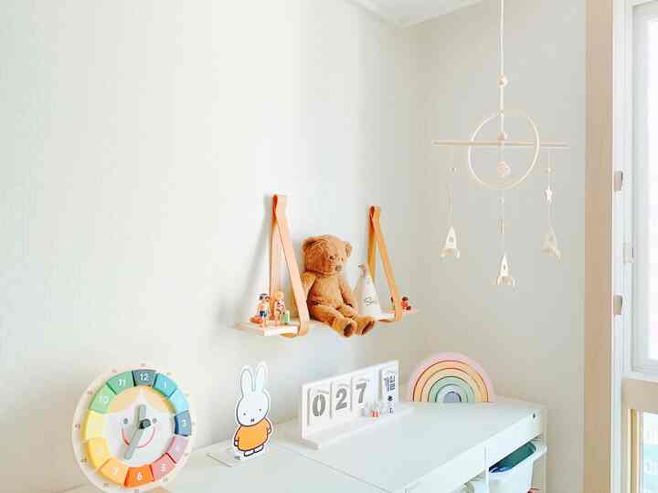 ホワイトとパステルカラーの調和が取れた子供部屋、壁に掛けられたモビールとテディベアが置かれた棚が印象的な明るく温かみのある空間