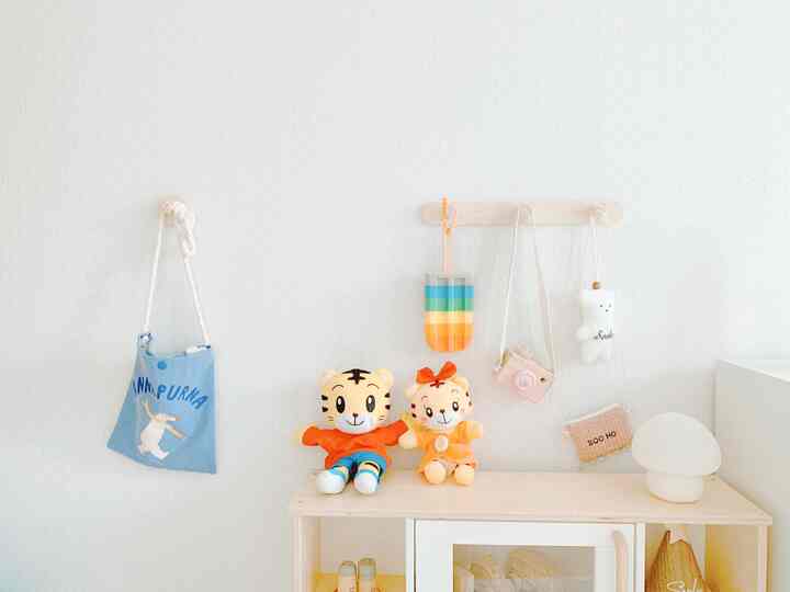Natural tones and white walls in a kids' room, featuring a wooden shelf and wall hooks with plush toys and bags creating a cozy atmosphere
