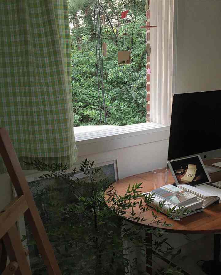 White and wood tone home office space featuring a window view of lush greenery, checkered curtain, and cozy desk setup