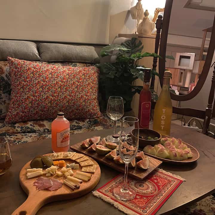 ナチュラルな色調の寝室、ソファベッドとワイングラスが置かれた木製のコーヒーテーブル、ヴィンテージカーペットと植物が調和した雰囲気のあるインテリア