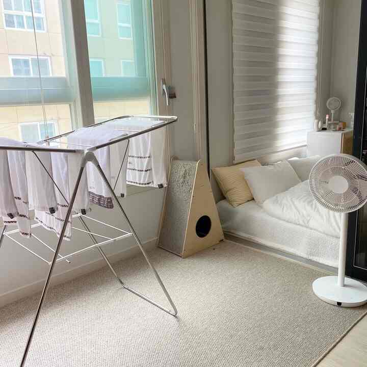 A modern bedroom space in white and beige tones featuring a laundry drying rack and a cat scratching post