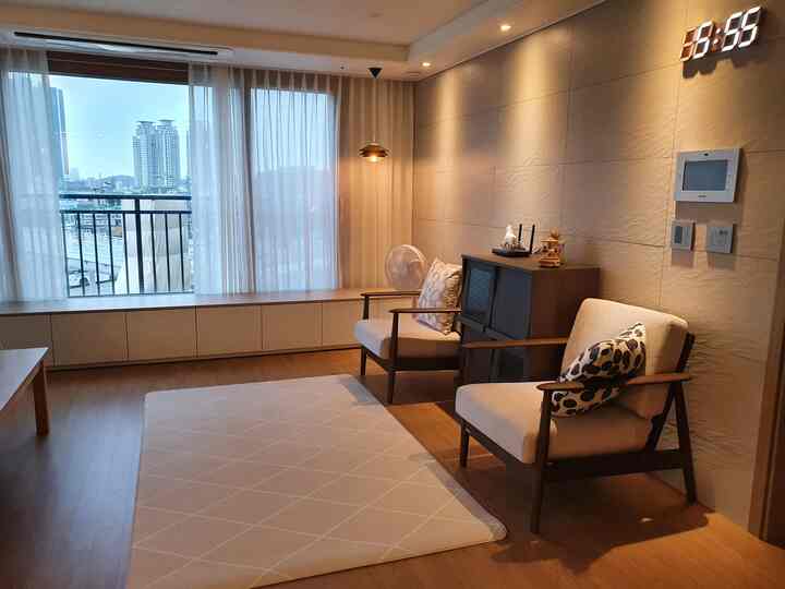 Natural and simple living room with wood-tone floor, beige armchairs, and white sheer curtains
