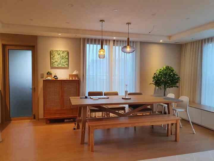 Natural wood tone dining room with white curtains, mid-sized dining table, bench, and chairs arranged in cozy space