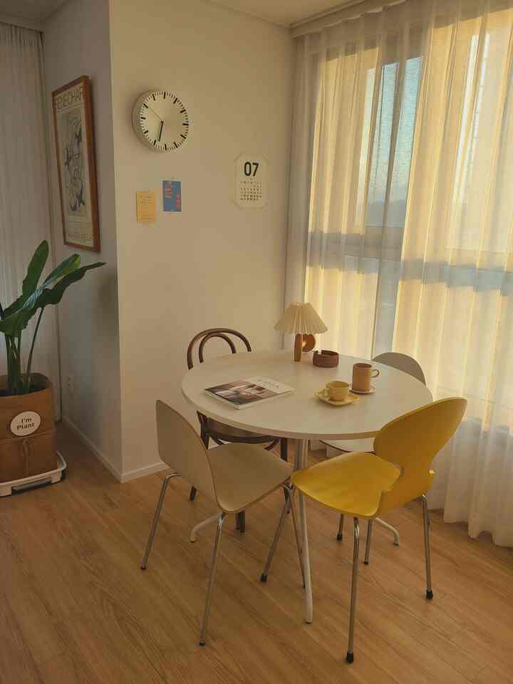Natural and simple dining room featuring a white round table with wood-tone flooring and a yellow accent chair