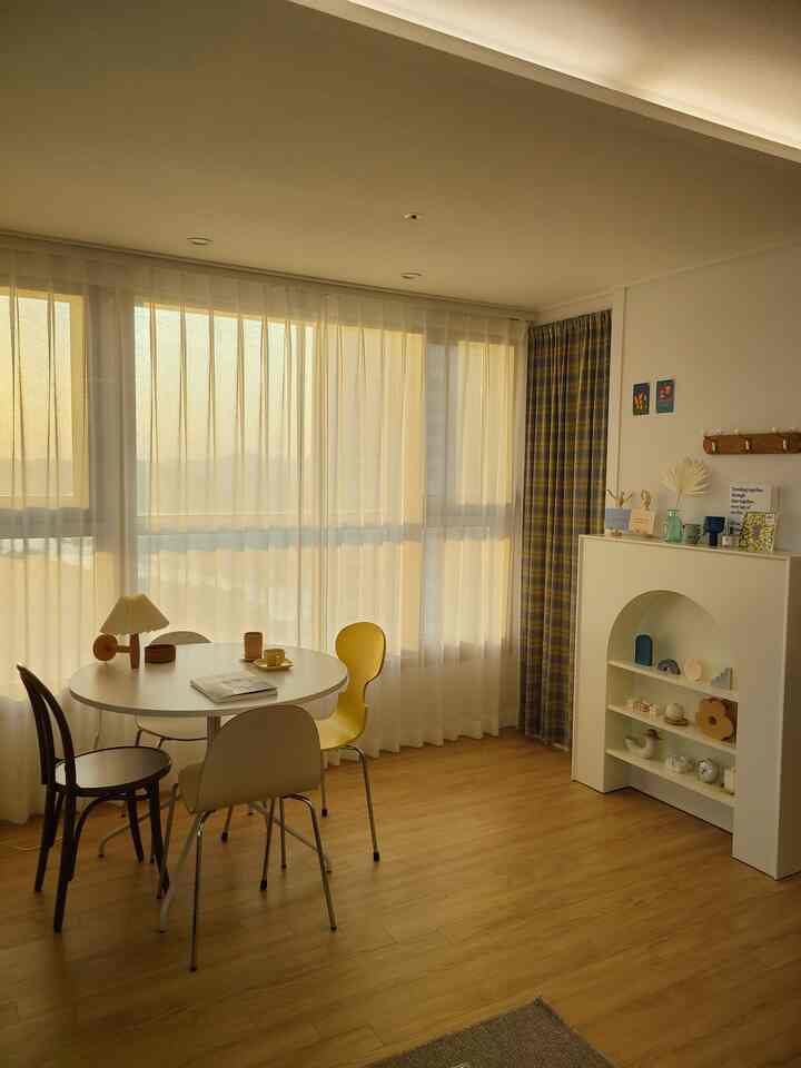 Warm wood-tone flooring dining room featuring white and yellow curtains with simple, natural atmosphere