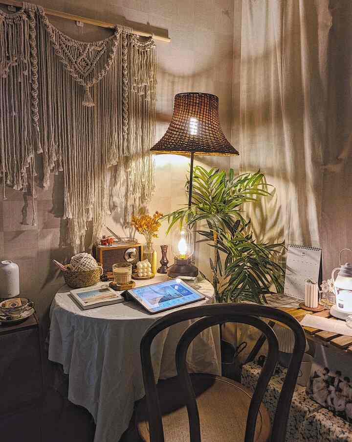 ナチュラルな色調の小さな部屋、テーブル上にラタンの照明とマクラメが配置された雰囲気のあるホームオフィス