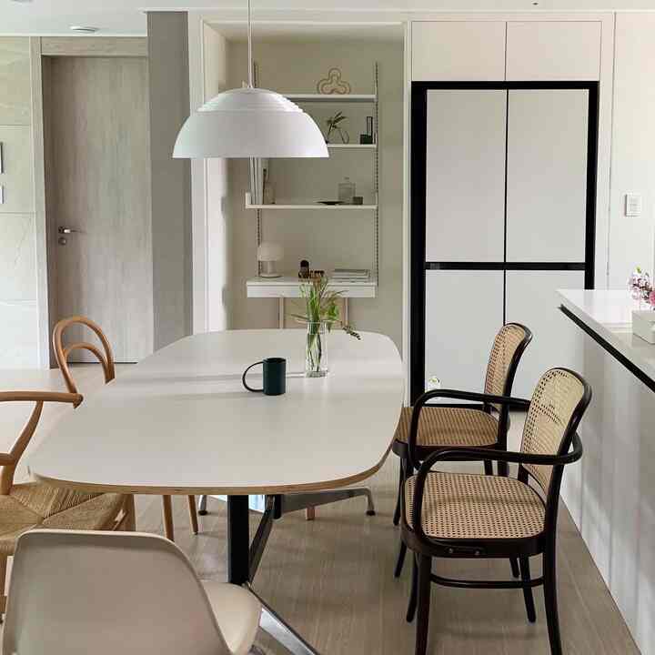 温かみのある白とナチュラルウッドのトーンのダイニング、ビスポーク冷蔵庫とペンダントライトが配置された居心地の良い空間