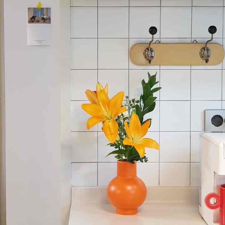 White tiled kitchen space featuring an orange vase with lilies, clean and bright atmosphere