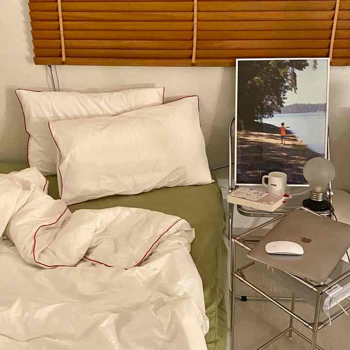 Modern bedroom featuring olive green mattress and white bedding, metal side table with laptop, books, and lamp creating cozy atmosphere