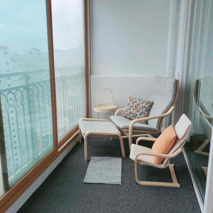White and wood tone veranda featuring two IKEA armchairs and a footstool in a simple and cozy setting