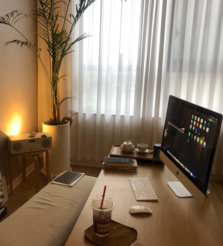Natural wood tones and white curtains define this compact home office space featuring an iMac and a coffee cup, creating a cozy atmosphere.