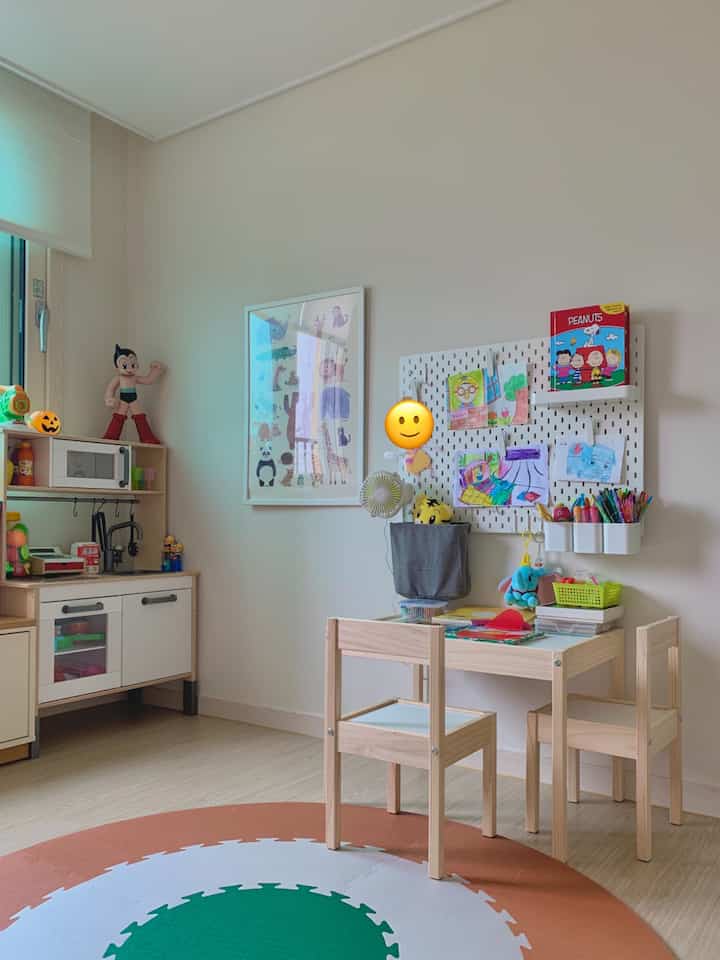 ベージュとウッドトーンの子供部屋、子供用デスクと椅子、壁のペグボードとおもちゃ収納が配置された雰囲気のある空間