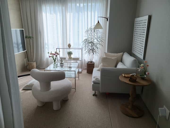 Natural color and white-toned living room featuring a unique armchair, sofa, and glass table in a cozy setting
