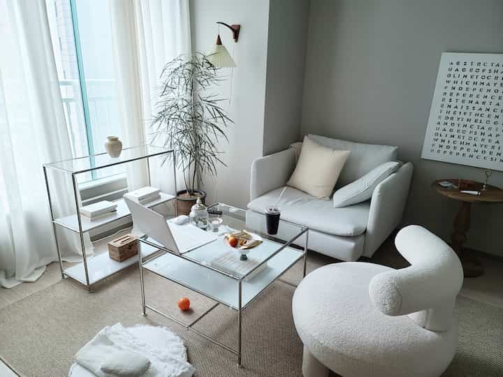 Natural beige and white toned living room featuring modern single sofa, armchair, and transparent glass table, creating a cozy atmosphere