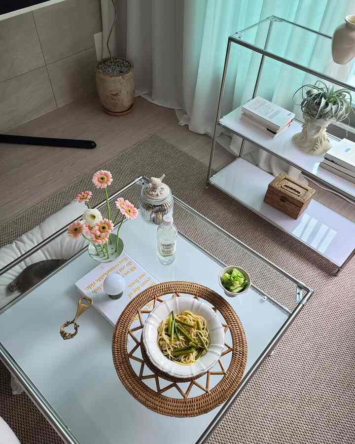 Natural toned living room featuring rattan placemat and transparent glass table with spaghetti and decor items creating cozy atmosphere