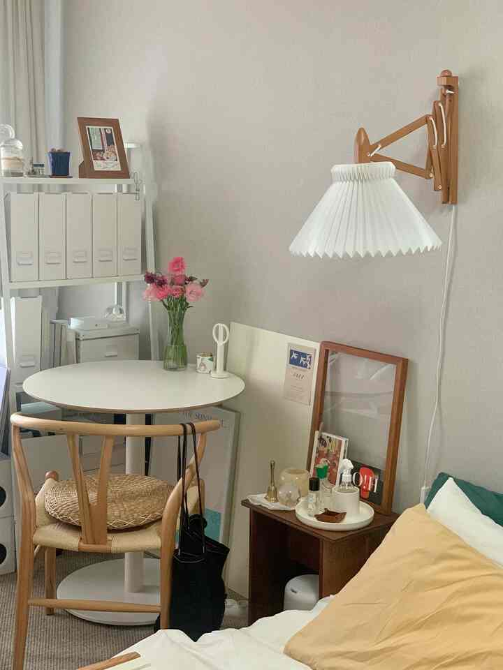 白と木目調の調和が取れたワンルーム寝室、コンパクトなレイアウトに収納ボックスと壁掛け照明が配置された落ち着いたインテリア