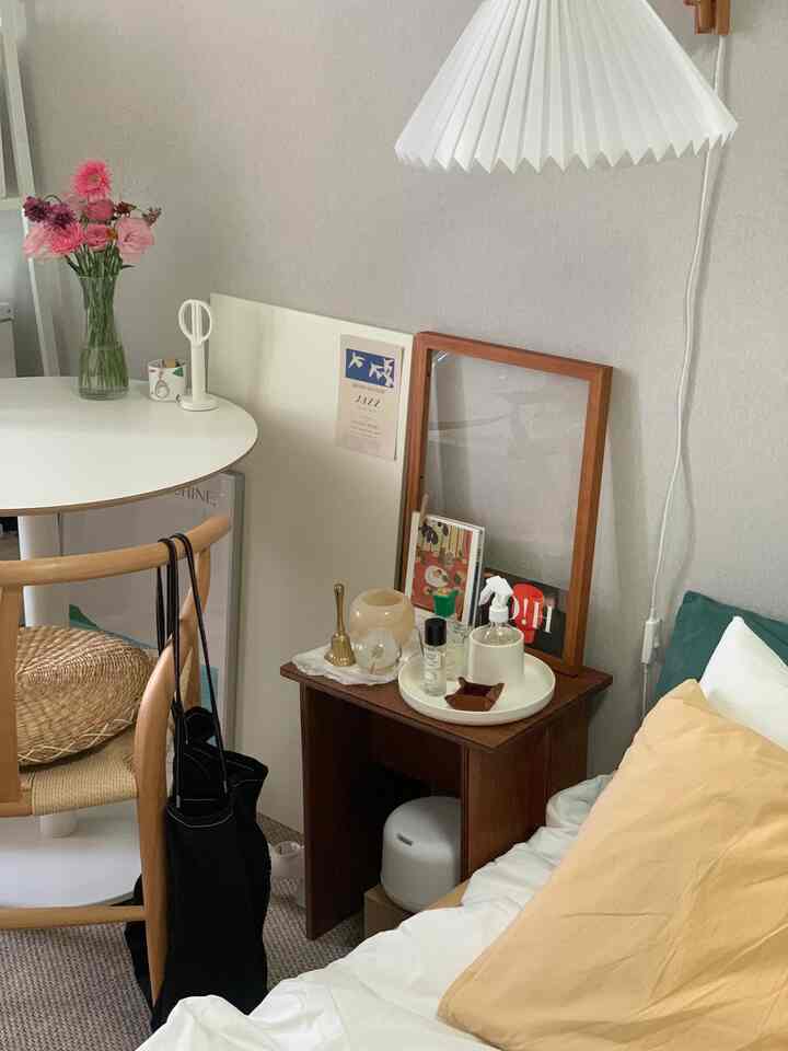 ホワイトと木目調が調和するナイトテーブルとダイニングテーブル、花瓶のある居心地の良い寝室兼ダイニングスペース