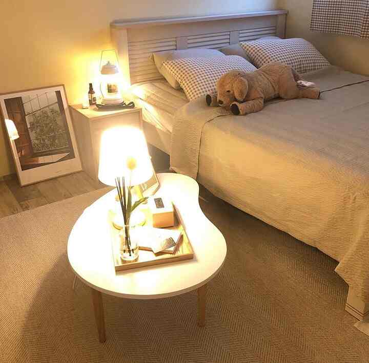 Beige and wood tone bedroom featuring a bed, coffee table, and nightstand lamp creating a cozy atmosphere