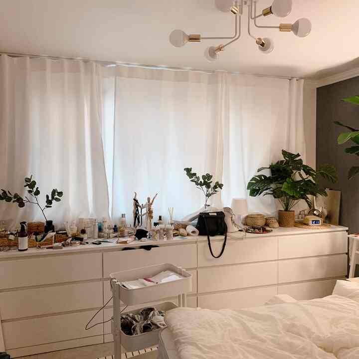 White and beige bedroom featuring large storage cabinet, curtains, natural decor elements, and plants creating a cozy atmosphere