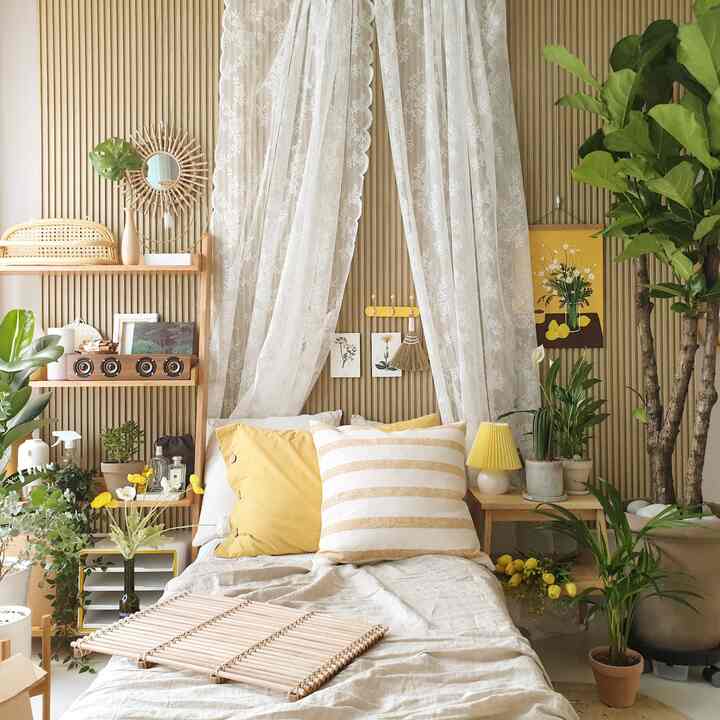 黄色のアクセントと木目調の壁が調和した寝室、さまざまな植物とレースカーテンが配置された雰囲気のあるインテリア
