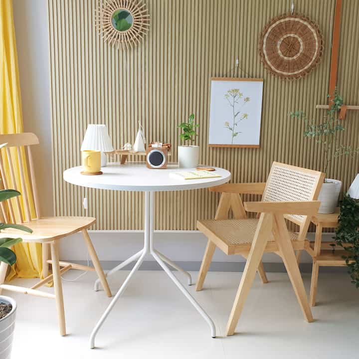 Bright white and wood tone living room featuring a round dining table with wooden and rattan chairs in a cozy natural setting