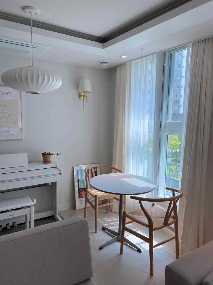 Bright white and wood tone living room corner featuring a round table and two W chairs positioned by the window, creating a warm natural modern space