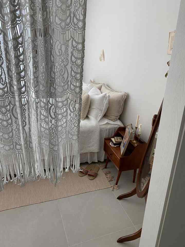 White and brown toned bedroom featuring lace curtain and vintage wooden nightstand creating a cozy atmosphere