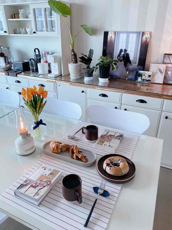 White and brown toned living room home cafe with dining table set featuring coffee, bread, books, and flowers creating a cozy vibe