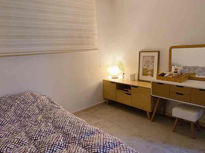 Natural modern guest room with white walls and beige carpet, featuring a bed, wooden console, and vanity creating a cozy atmosphere