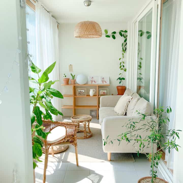 明るいホワイトとナチュラルウッドのベランダ、ソファとラタンチェア、植物が配置された雰囲気のあるインテリア