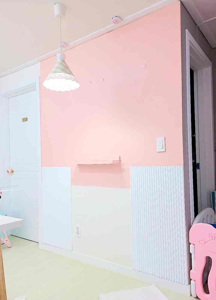 Pink and white toned kids' room featuring a pink wall and safety gate with a clean, simple atmosphere