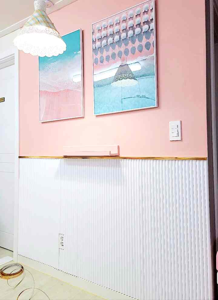 ピンクと白の壁にゴールドのモールディングが配されたインテリア、ペンダントライトと額縁が印象的な空間