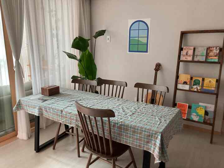 White and brown toned living room featuring dining table, chairs, bookshelf, and plant with warm home cafe vibe