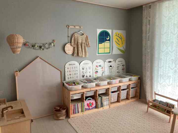 Natural toned kids' room with gray walls and white lace curtains, featuring tidy toy storage and a soft patterned rug