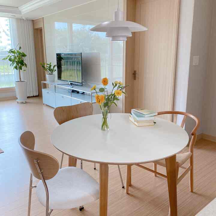 白と木目調が調和するリビング、円形のダイニングテーブルと椅子、ペンダントライトが清潔感のあるナチュラルモダンな雰囲気を演出する空間