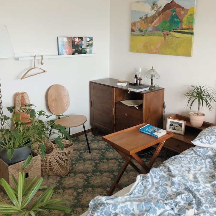 Natural tone bedroom featuring wooden furniture, rug, and multiple plants creating a cozy atmosphere