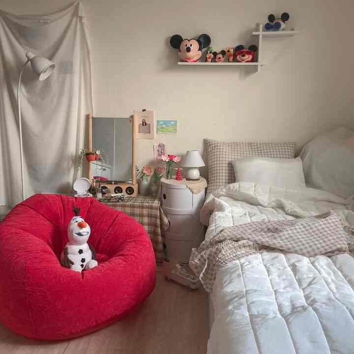Pastel and natural toned studio bedroom featuring a vivid red bean bag sofa and cozy bedding creating a warm atmosphere