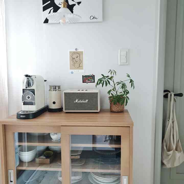 白い壁と木目調キャビネットが配置されたキッチンのおうちカフェ空間、コーヒーマシンとスピーカー、植物が温かみを演出