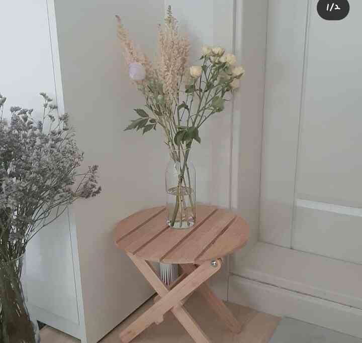 Natural wood tone small round table with a transparent glass vase and dried flowers in a simple entrance space