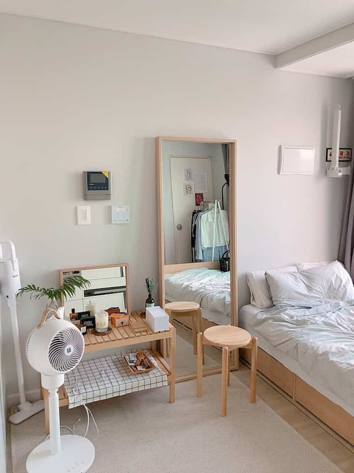 Beige and natural wood-tone studio bedroom featuring wooden stools and a large standing mirror with a cozy, clean atmosphere