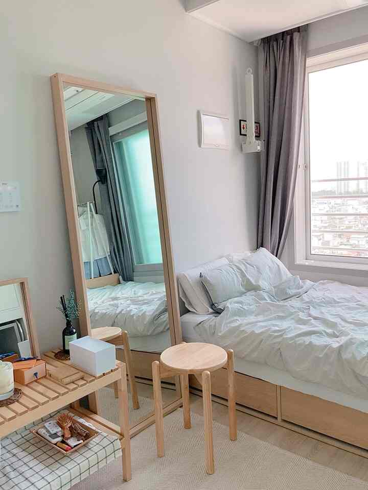 Cozy small bedroom with natural wood tones and white colors, featuring a large standing mirror and a wooden stool