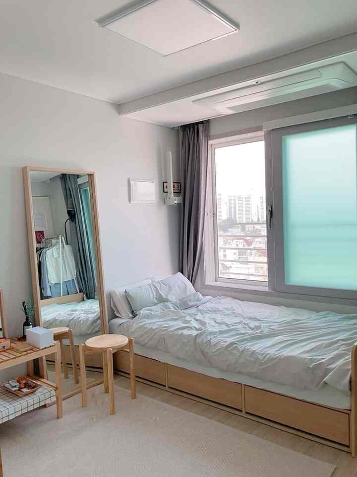 Bright white and wood-tone compact bedroom for single household featuring storage bed and full-length mirror with natural atmosphere