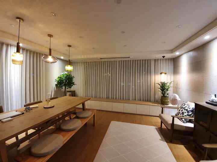 Warm wood tones and white curtains characterize this living and dining room featuring natural plants and simple lighting for a cozy atmosphere
