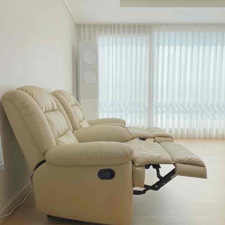 Beige-toned living room in a studio apartment featuring reclining sofa and sheer curtains for a natural interior