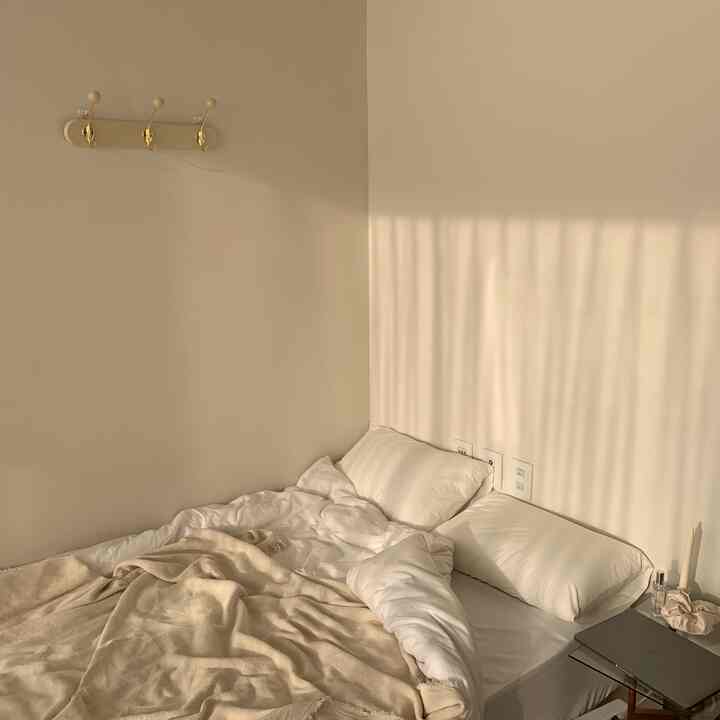 A cozy and clean bedroom in white and beige tones featuring a coat rack and candles on the nightstand