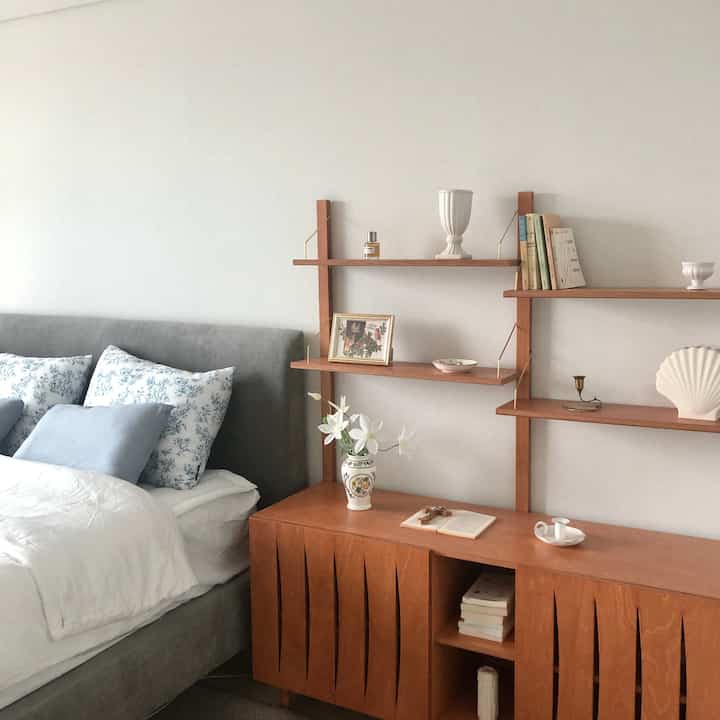 Natural style bedroom with white walls, wood tone shelves, and a gray bed