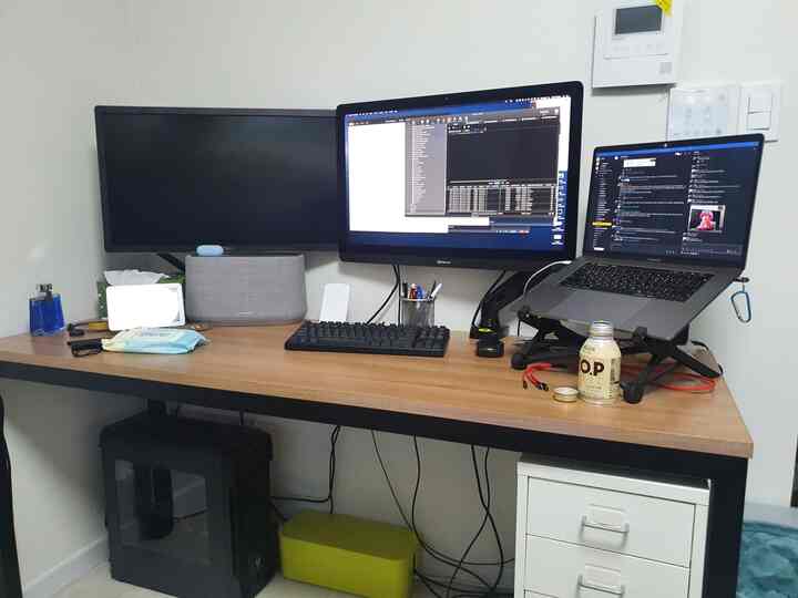 明るいブラウンのデスクが置かれたコンパクトなホームオフィス、デュアルモニターとノートパソコンを備えたリモートワーク環境