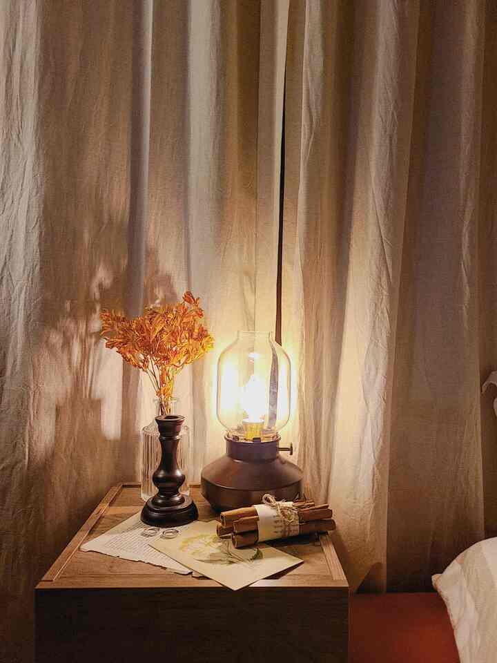 温かみのあるベージュ色調の寝室、ナイトテーブルにヴィンテージ風の照明と花瓶、シナモンスティックが置かれ、落ち着いた雰囲気のインテリア