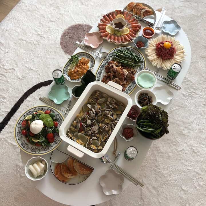 Light beige carpeted dining area with white oval table featuring assorted bowls, plates, and cutlery arranged for a meal gathering
